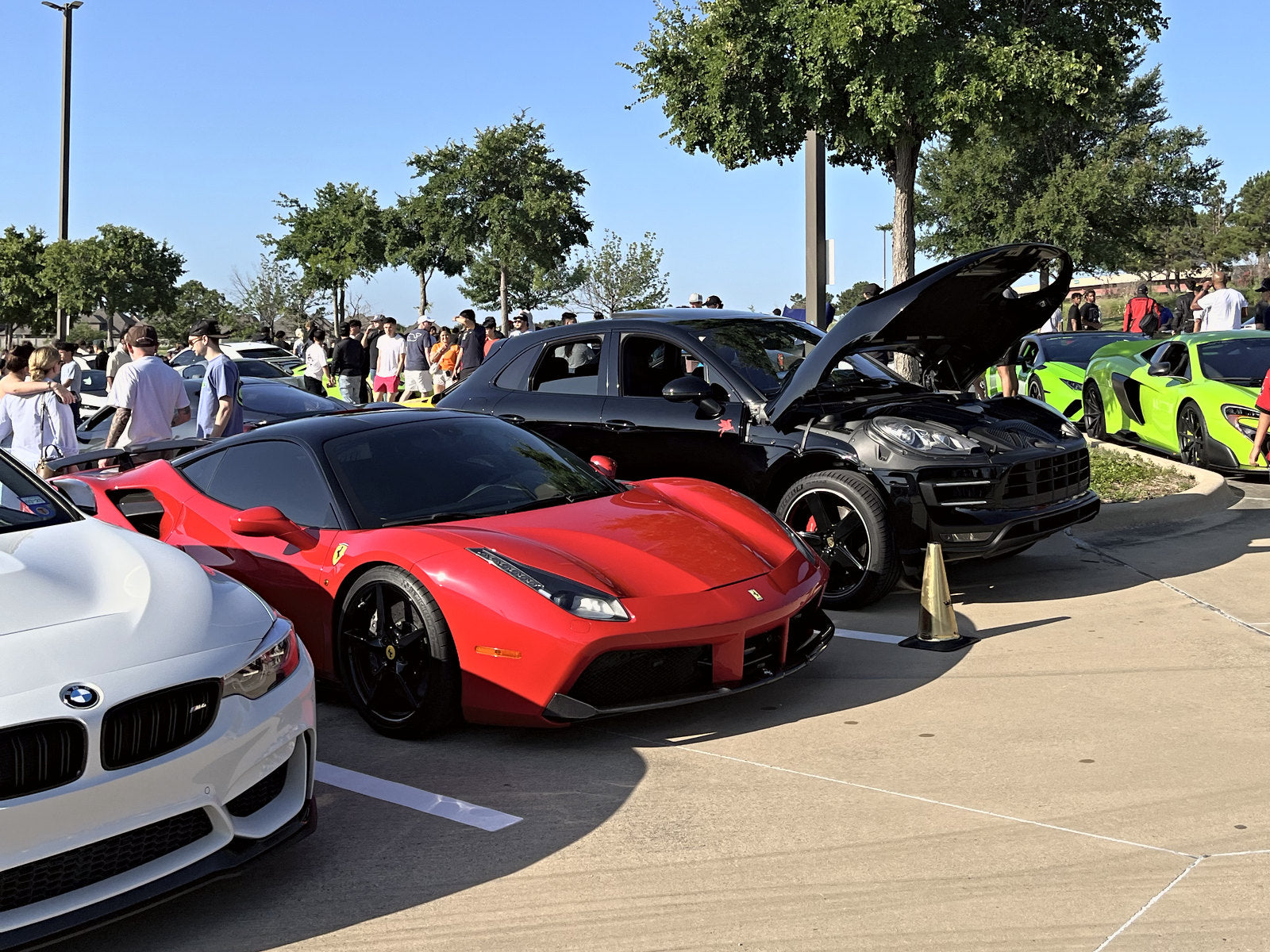A red mid-engine supercar in a row of cars, a black one with its doors open behind it
