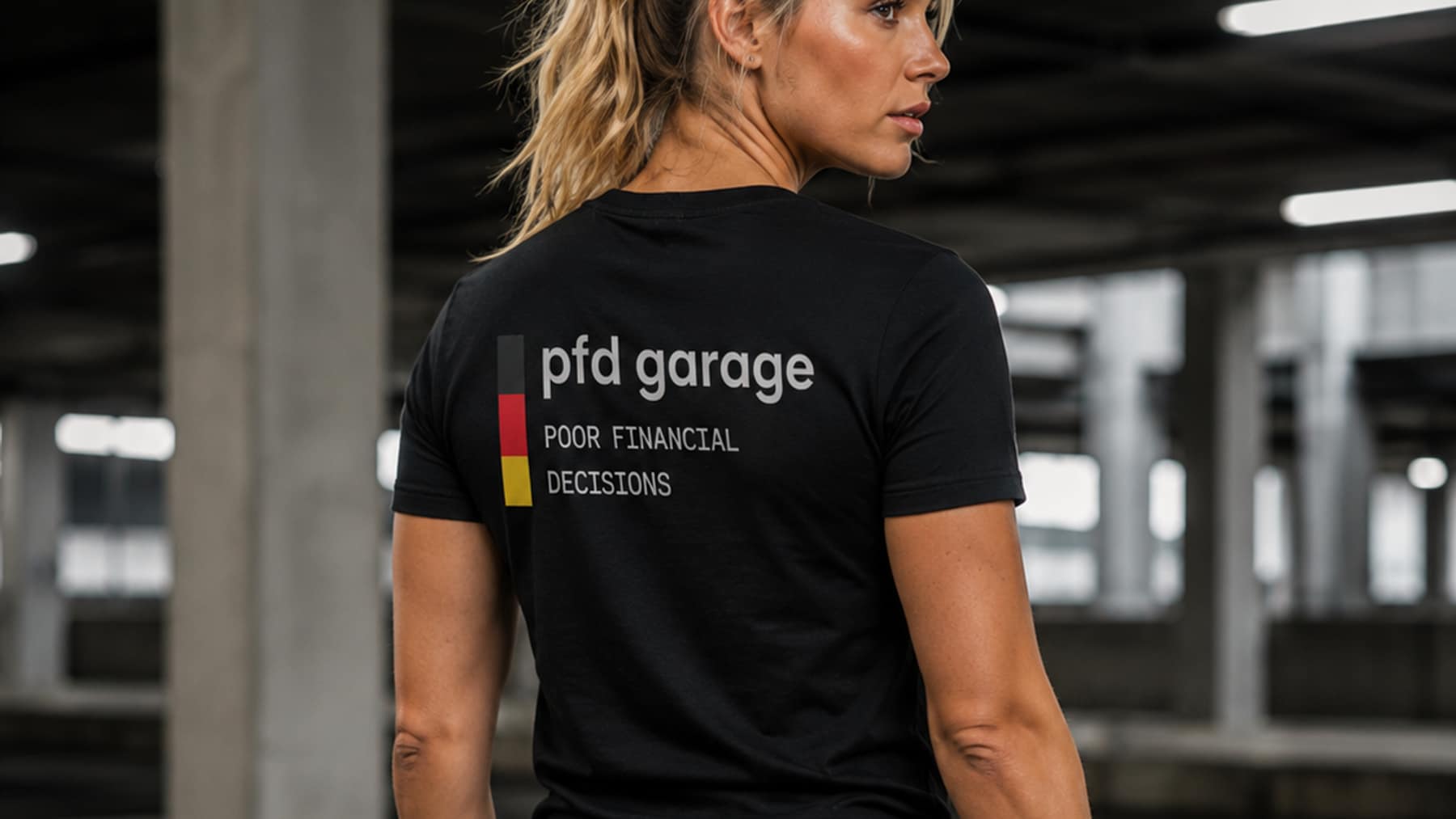 Back view of a black tee printed with the pfd garage wordmark and a black, red and yellow bar, worn in a parking garage