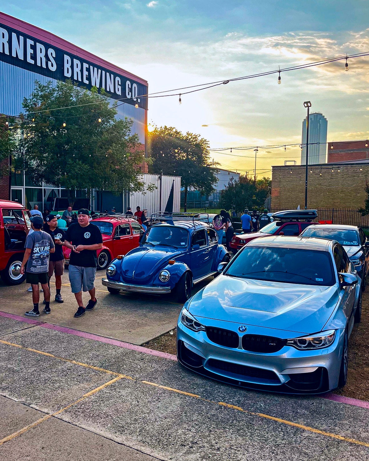 A silver sports coupe and classic cars parked outside a brewery at a weekend car meet
