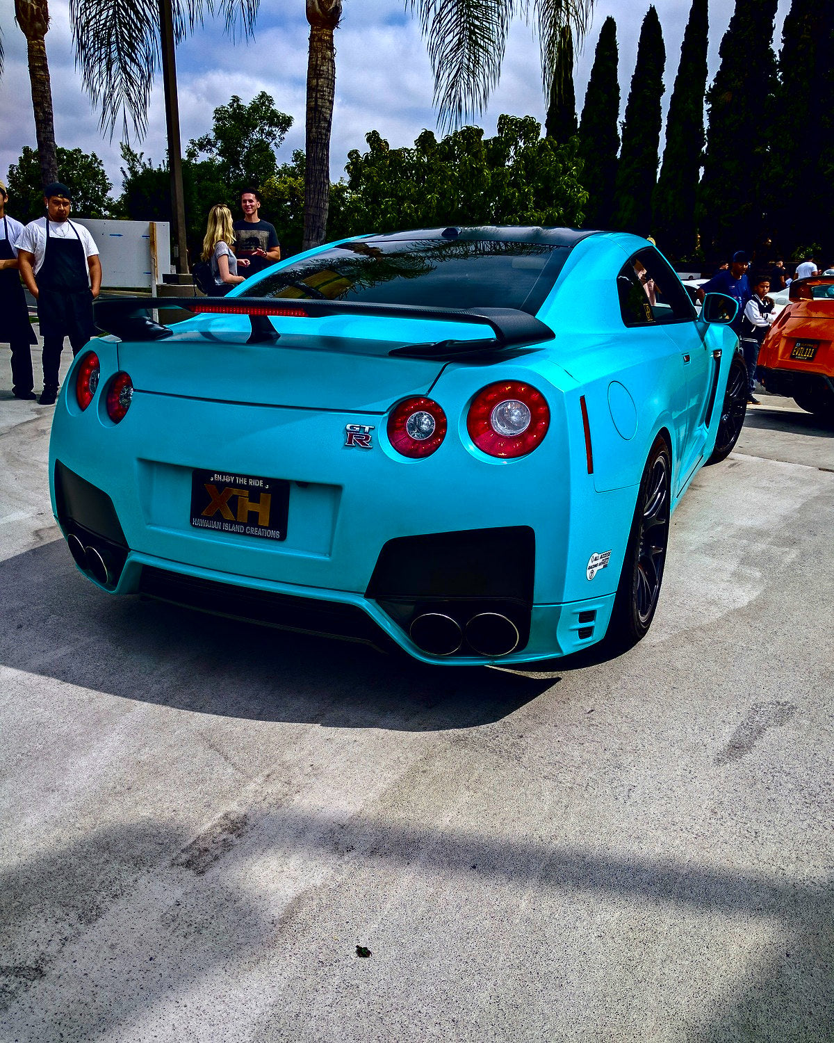 A teal R35 from behind at a busy street meet, people gathered on the sidewalk