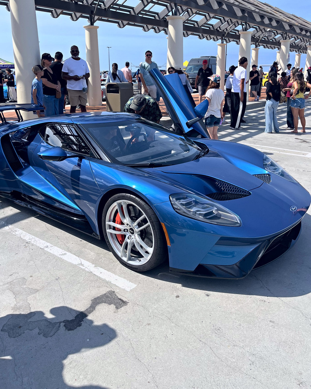 A blue mid-engine supercar parked under a pavilion, people gathered around