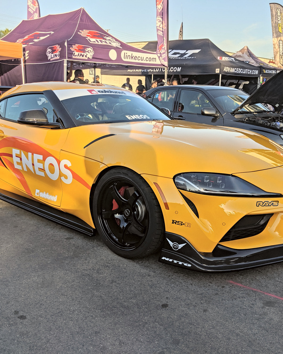 A yellow A80 in race livery under the event tents at a race weekend