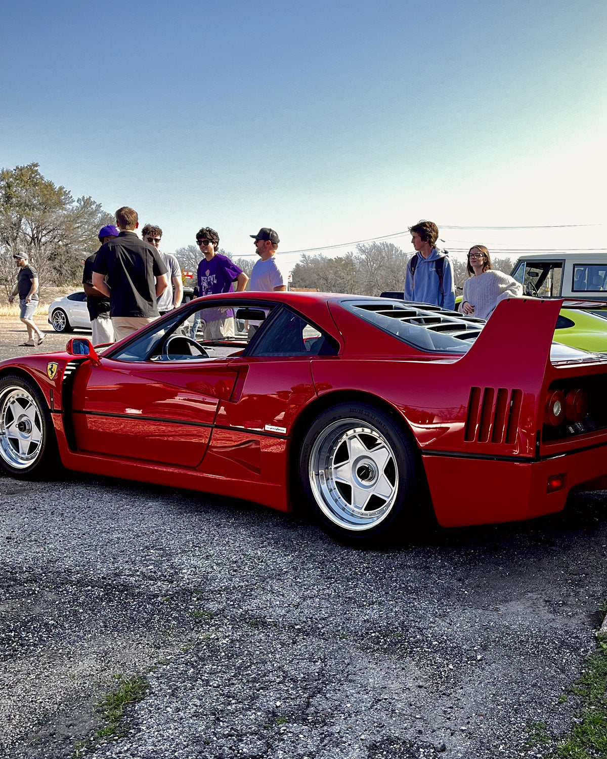 A red mid-engine supercar with its rear wing up, a group of people talking beside it