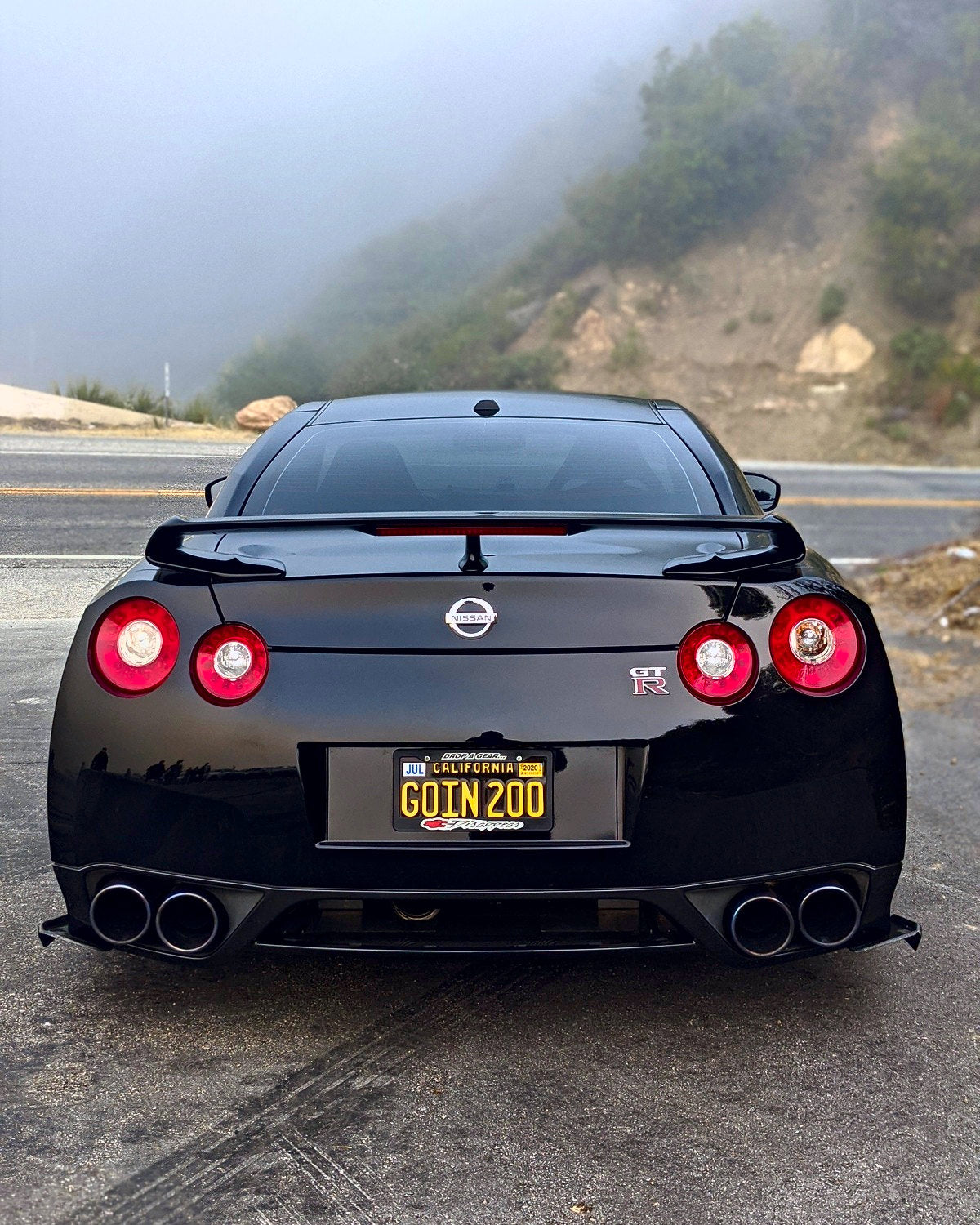 A black R35 from straight behind, quad exhausts glowing, fog rolling over the hills