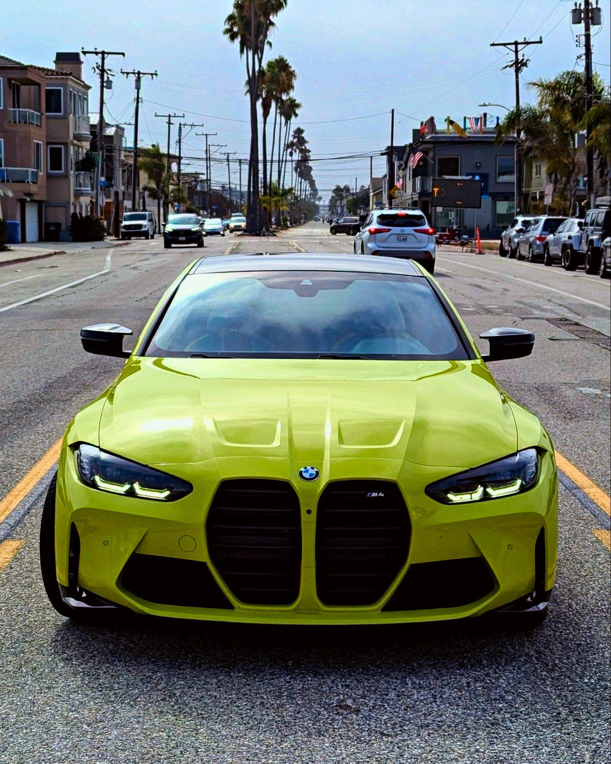 A lime green G82 head-on in the middle of a palm-lined street
